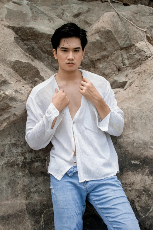 a man in a white shirt leaning against a rock, inspired by Zhang Han, lean man with light tan skin, ramil sunga, wearing a linen shirt, non binary model