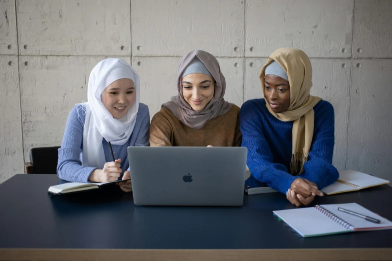 three women sitting at a table looking at a laptop, hurufiyya, microsoft, photo of a classroom, islamic, multicoloured