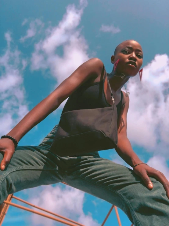 a man standing on top of a metal structure, by Nathalie Rattner, trending on pexels, afrofuturism, wearing a black cropped tank top, beautiful androgynous girl, with clouds in the sky, brown buzzcut