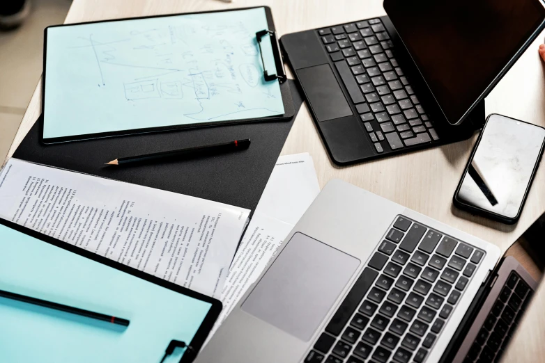 a group of laptops sitting on top of a wooden table, technical document, black and teal paper, writing on a clipboard, thumbnail