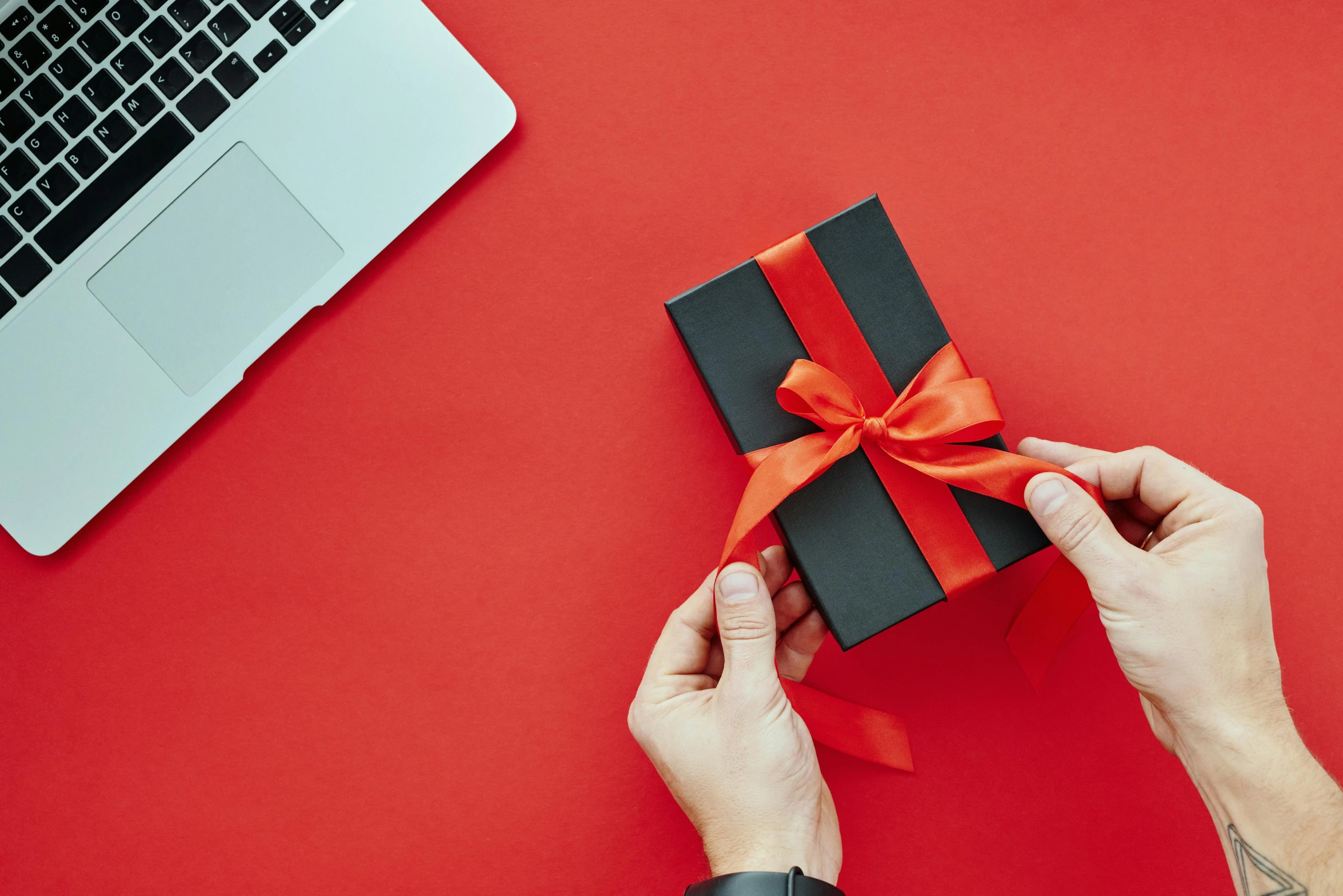 a person holding a gift in front of a laptop, by Julia Pishtar, pexels contest winner, black and red only, packaging, red ribbon, thumbnail