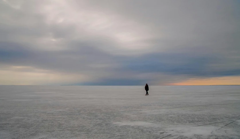 a person walking across a snow covered field, inspired by Scarlett Hooft Graafland, unsplash contest winner, gazing off into the horizon, white sea cloud, gray wasteland, ice seracs