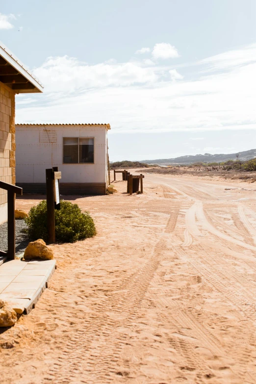 a house sitting on the side of a dirt road, les nabis, flat wastelands, exterior, sandy beach, rustic