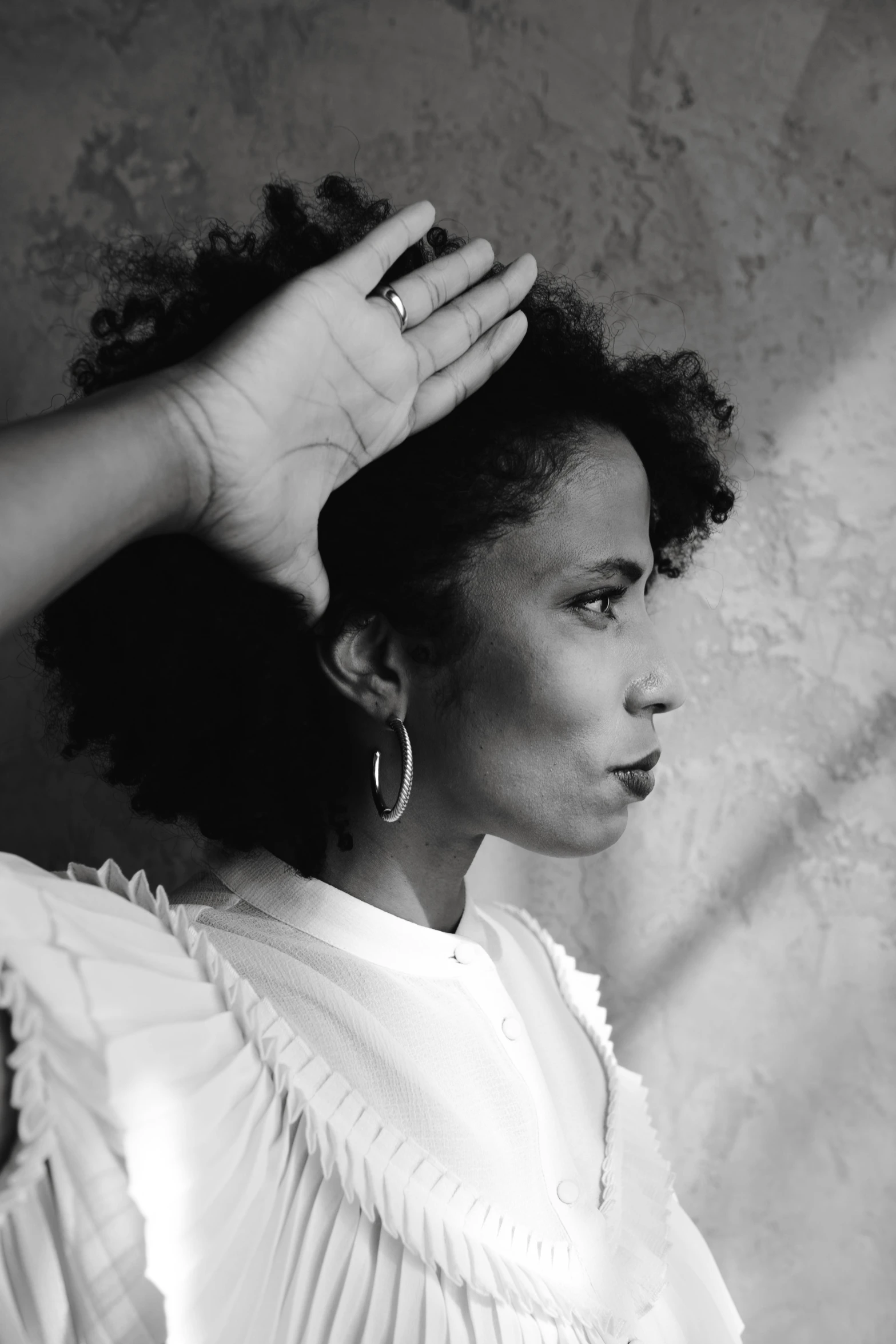 a black and white photo of a woman with her hand on her head, inspired by Carrie Mae Weems, voluminous sleeves, slightly sunny, curly afro, promotional image