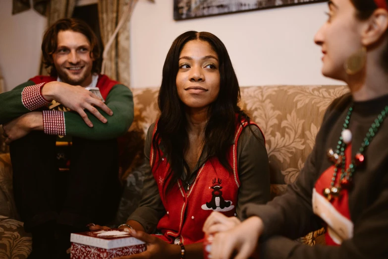 a group of people sitting on top of a couch, by Emma Andijewska, pexels contest winner, wearing a red gilet, giving gifts to people, card game, tessa thompson