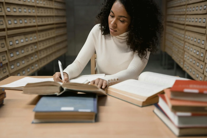 a woman sitting at a table writing in a book, trending on pexels, academic art, grand library, casually dressed, black, an olive skinned