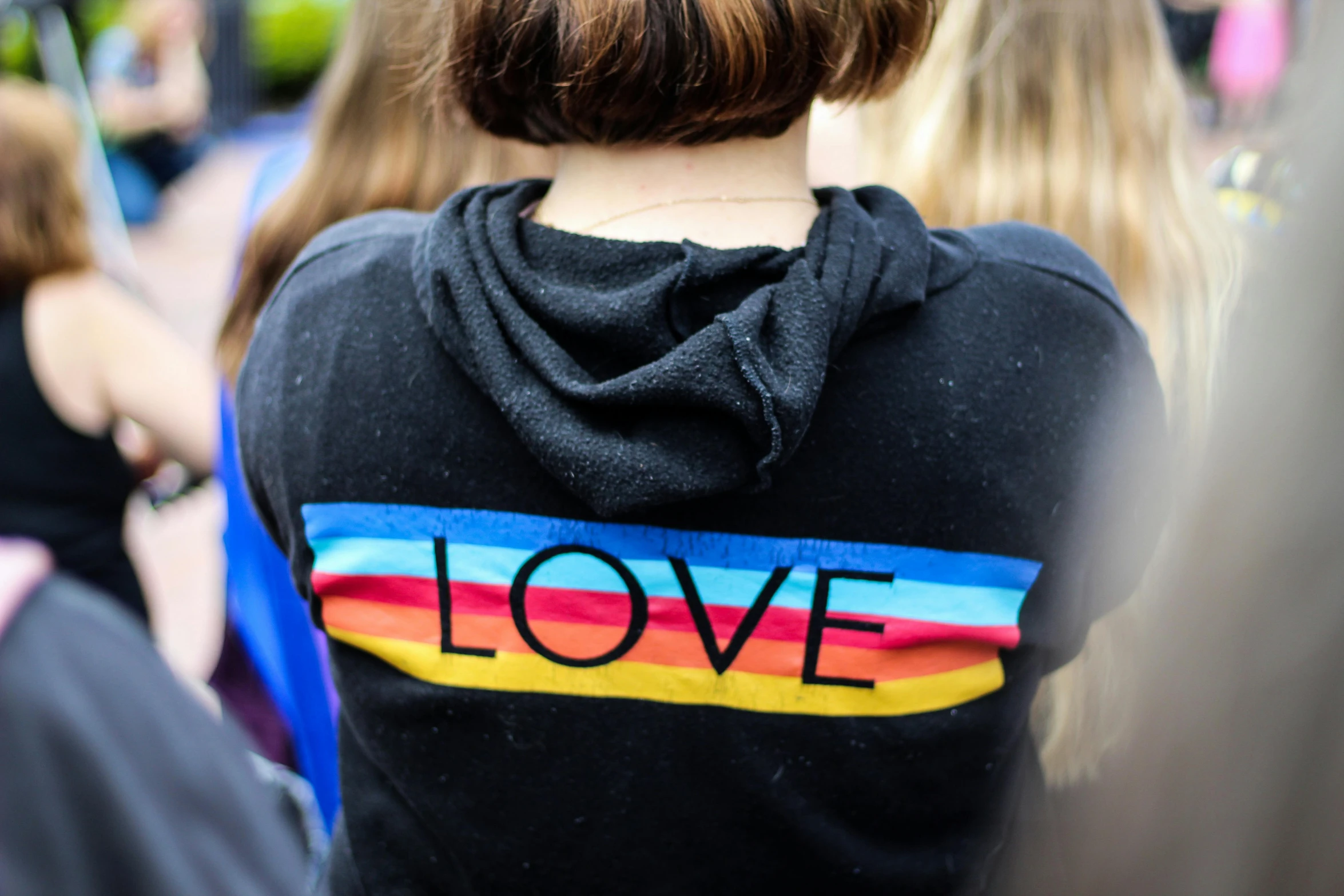 a woman wearing a hoodie with the word love on it, lgbtq, from the back, photo from a spectator, girls