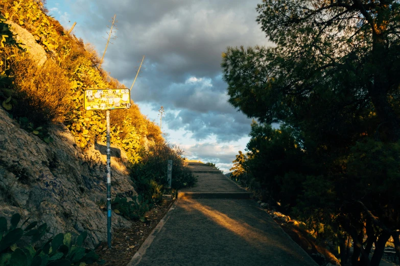 a street sign sitting on the side of a road, a picture, unsplash, cliff side at dusk, costa blanca, pathway, on a hill