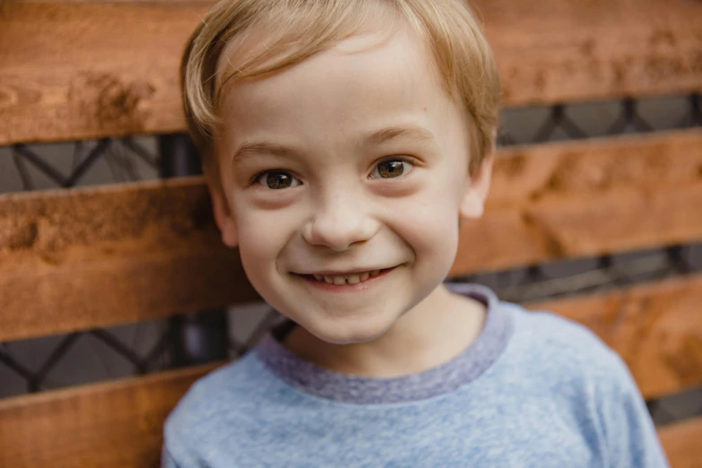 a young boy sitting on top of a wooden bench, smiling at the camera, zoomed in, avatar image, andrew tate