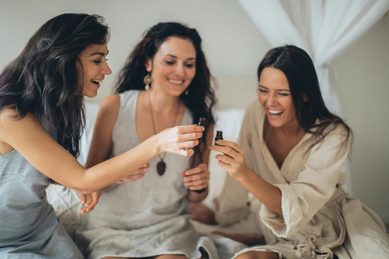 a group of women sitting on top of a bed, trending on pexels, carrying a bottle of perfume, manuka, laughter, brunette