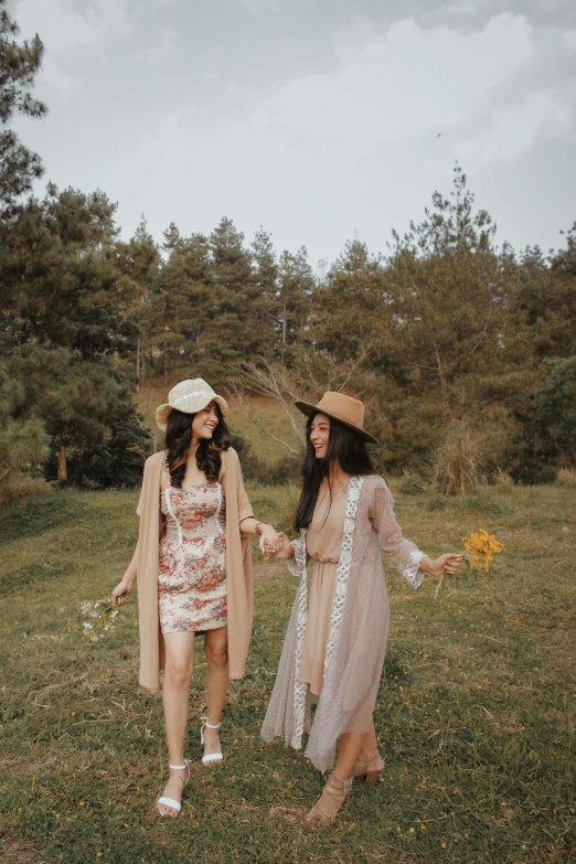 two women standing next to each other in a field, a picture, trending on pexels, wearing robe, with hat, lookbook, holding hand