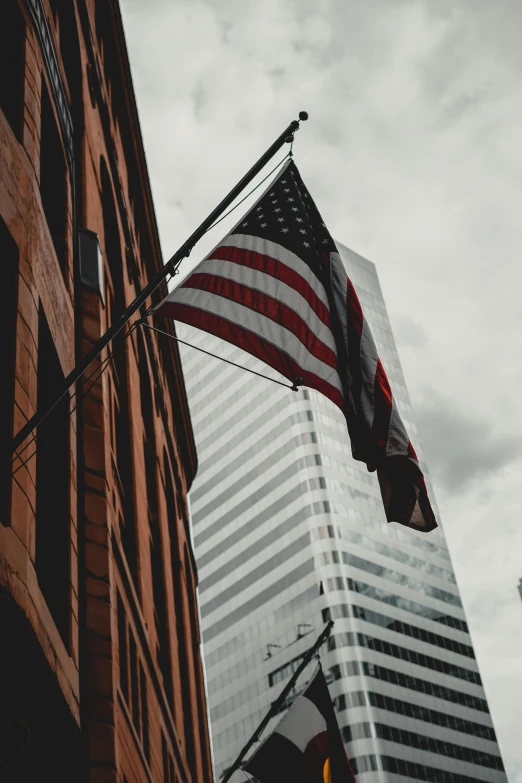 an american flag flying in front of a tall building, a picture, unsplash contest winner, 🚿🗝📝, tradition, desaturated, minn