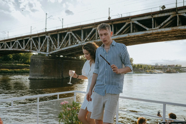 a man and a woman standing next to a river, pexels contest winner, happening, holding a glass of wine, neo kyiv, holding a baguette, bridge