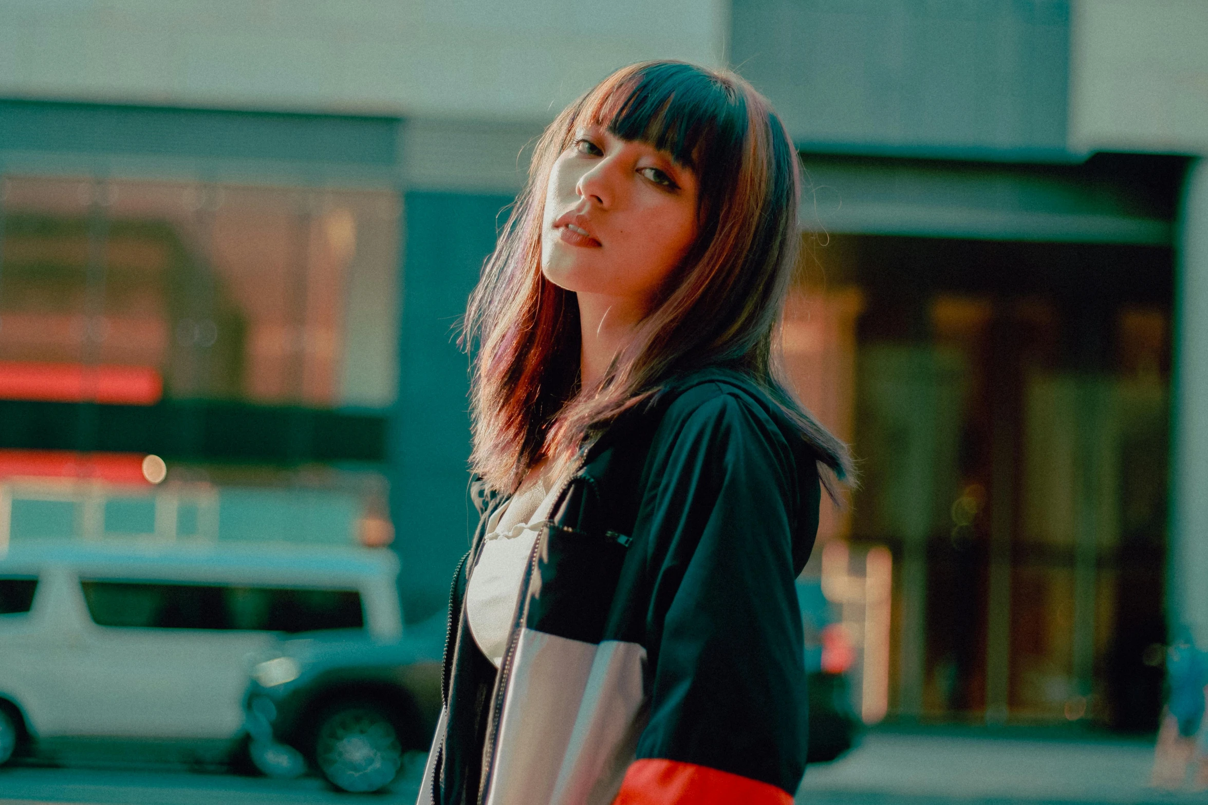 a woman holding a red frisbee on a city street, an album cover, inspired by Elsa Bleda, pexels contest winner, realism, long dark hair with bangs, in a black hoodie, looking from side, wearing a track suit