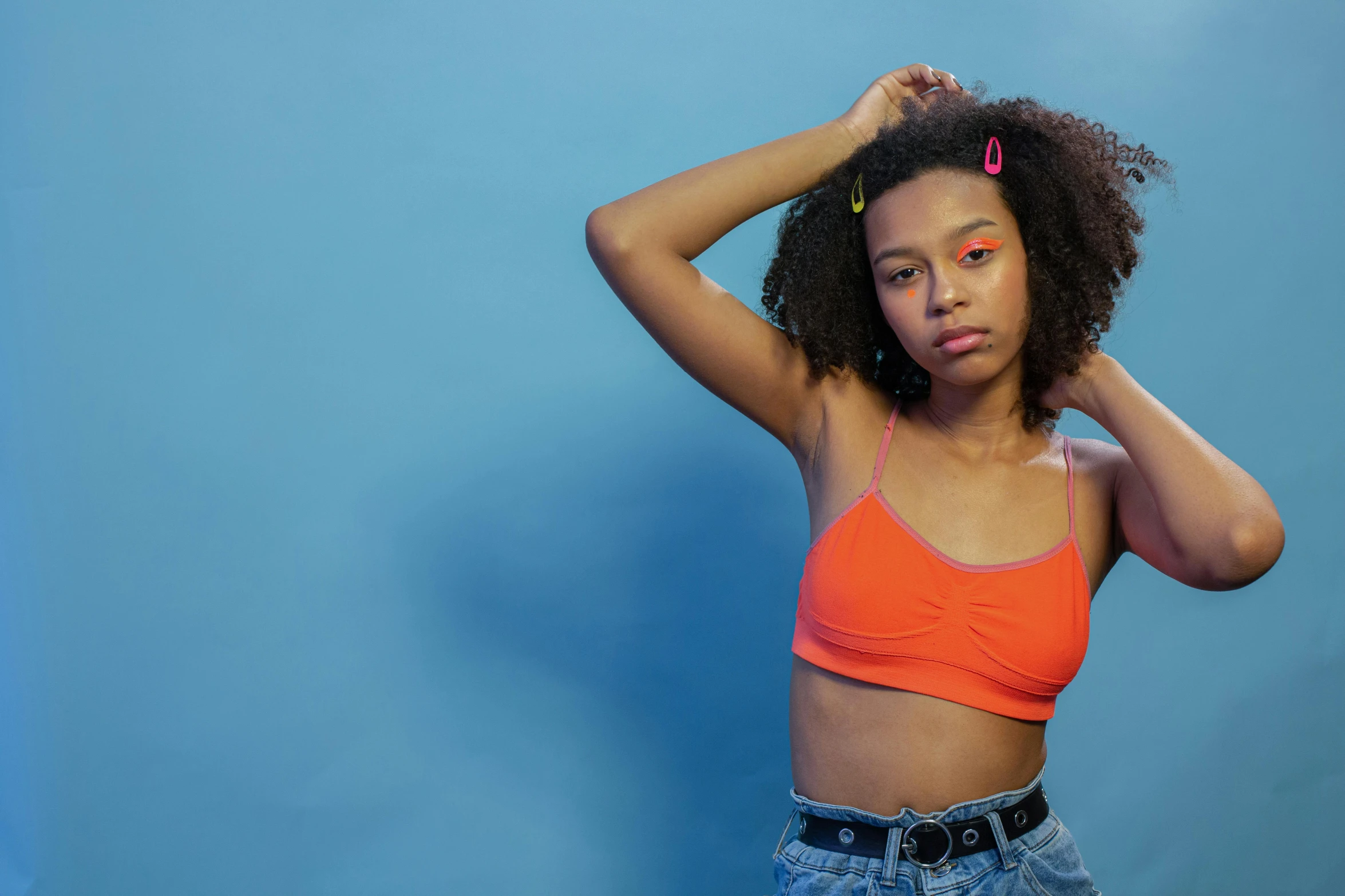 a woman standing in front of a blue wall, inspired by Gustave Boulanger, trending on pexels, orange halter top, black teenage girl, soft neon, mixed race woman