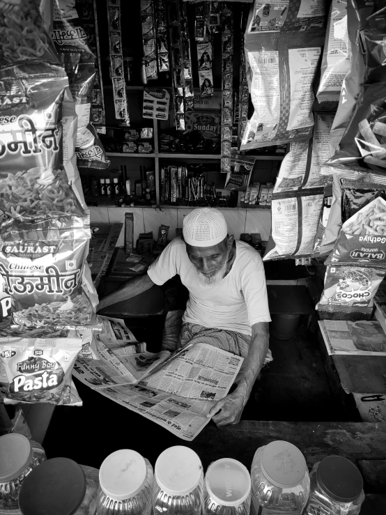 a black and white photo of a man reading a newspaper, by Peter Churcher, pexels contest winner, food stall, ranjit ghosh, convenience store, by greg rutkowski