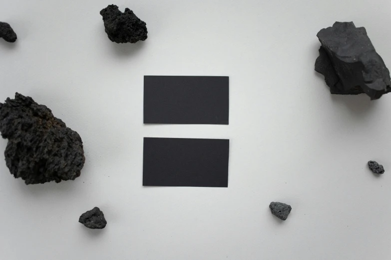 a group of black rocks sitting on top of a white surface, cardstock, rectangle, carbon, lunar color palette