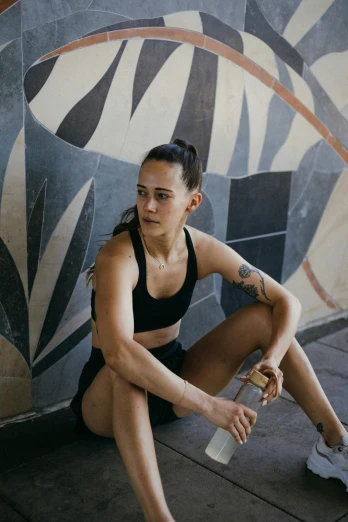 a woman sitting on the ground next to a skateboard, a portrait, by Jessie Alexandra Dick, tight black tank top and shorts, anjali mudra, looking serious, on a wall