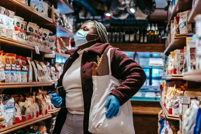 a woman wearing a face mask in a grocery store, by Julia Pishtar, pexels, dark-skinned, bag over the waist, 🦩🪐🐞👩🏻🦳, standing in township street