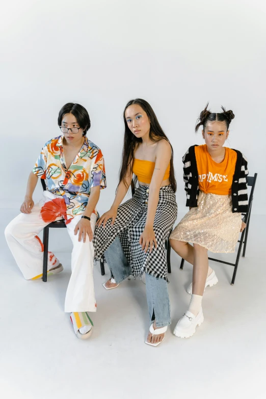 a group of people sitting next to each other, an album cover, unsplash, gutai group, patterned clothing, white and orange, asian women, sitting on a stool