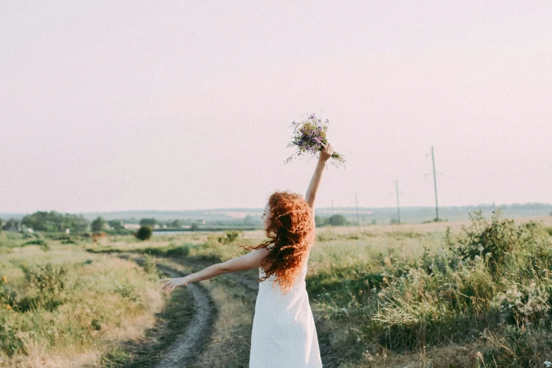 a woman standing on a dirt road holding a bunch of flowers, pexels contest winner, redhead girl, girl in white dress dancing, imagining a blissful fate, rule for thirds