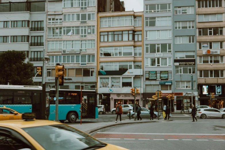 a yellow taxi driving down a street next to tall buildings, a photo, by Matija Jama, pexels contest winner, people waiting in bus stop, belgium, street of teal stone, square