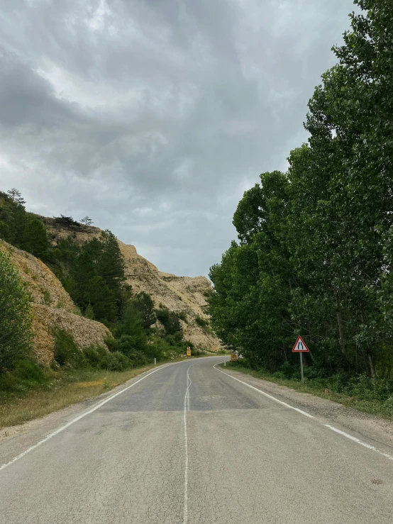 a motorcycle is parked on the side of the road, chalk cliffs above, photo of džesika devic, hill with trees, thumbnail