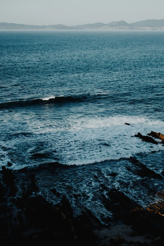 a man riding a surfboard on top of a wave in the ocean, inspired by Elsa Bleda, pexels contest winner, minimalism, with lots of dark grey rocks, deep blue sea color, today\'s featured photograph 4k, slide show