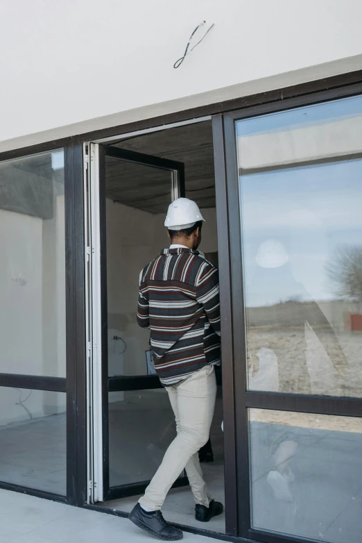 a man in a hard hat is entering a building, pexels contest winner, modernism, big french door window, full body framing, standing outside a house, inspect in inventory image