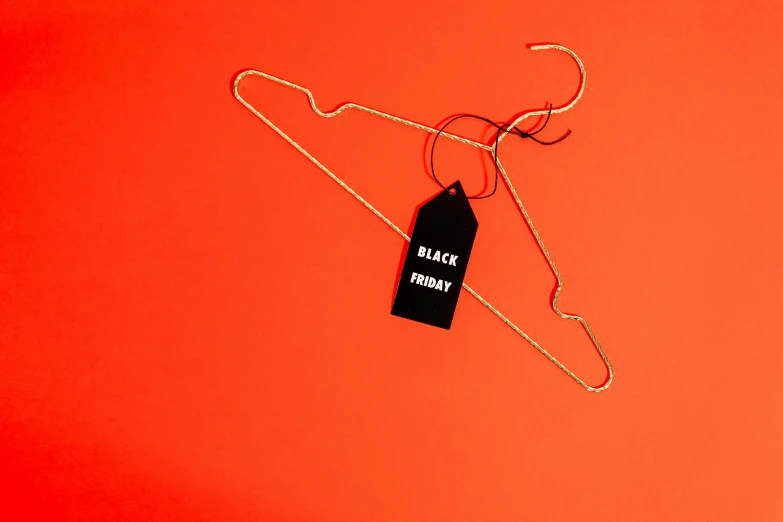 a hanger with a black label on a red background, by Julia Pishtar, pexels, hurufiyya, holiday season, black skin, orange and black tones, image of the day