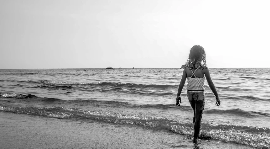 a black and white photo of a woman walking on the beach, by Mathias Kollros, pexels, little girl, in the sea, young girl, illustration »