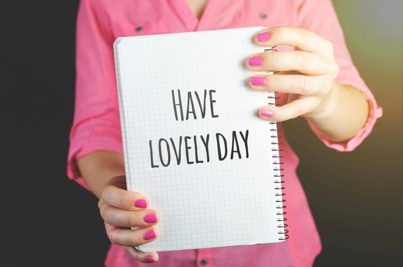 a woman holding a notebook with the words have lovely day written on it, pixabay, pink, consistency, regular sized, waving