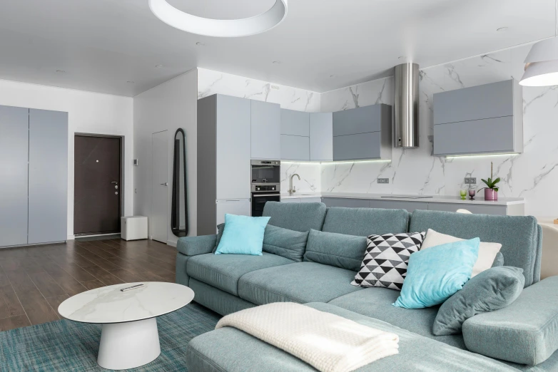 a blue couch sitting in a living room next to a kitchen, a 3D render, by Adam Marczyński, unsplash contest winner, light and space, white grey color palette, rounded ceiling, white and teal metallic accents, small and cosy student bedroom