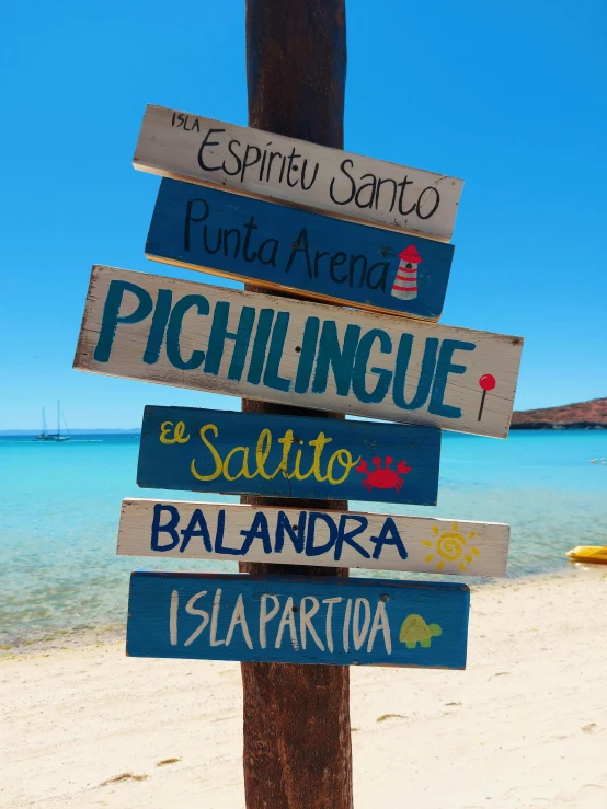 a wooden sign sitting on top of a sandy beach, art & language, spanish, profile image, islands, on the ocean