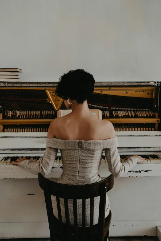 a woman sitting on a chair in front of a piano, on a white table, portrait featured on unsplash, from back, ornately dressed