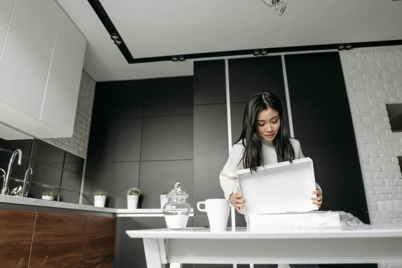 a woman sitting at a kitchen table with a laptop, pexels contest winner, standing on a desk, glossy white, cardboard, ( mechanical )