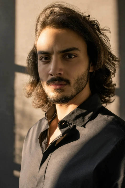 a man with long hair wearing a black shirt, inspired by Camilo Egas, groomed facial hair, raden saleh, profile image, actress