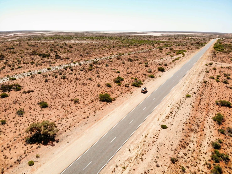 a car driving down the middle of a desert road, by Lee Loughridge, unsplash, hurufiyya, on a hot australian day, aerial, thumbnail, david normal