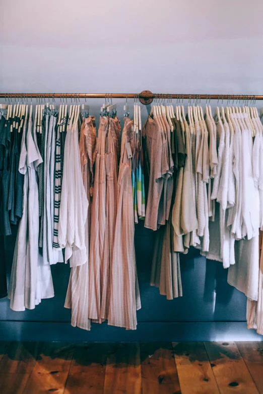 a rack of clothes sitting on top of a wooden floor, a colorized photo, by Jessie Algie, trending on unsplash, renaissance, pastel pink robes, muted browns, stores, wearing a camisole and shorts