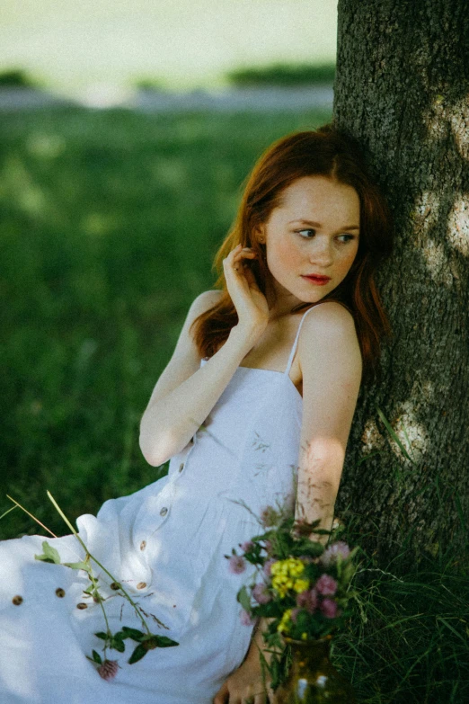 a woman in a white dress sitting under a tree, sadie sink, shot with sony alpha 1 camera, portrait image