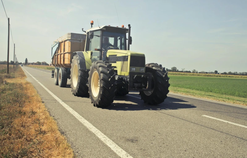 a tractor pulling a trailer down a rural road, by Andries Stock, pixabay, massive wide trunk, hexagonal shaped, very asphalt, corn