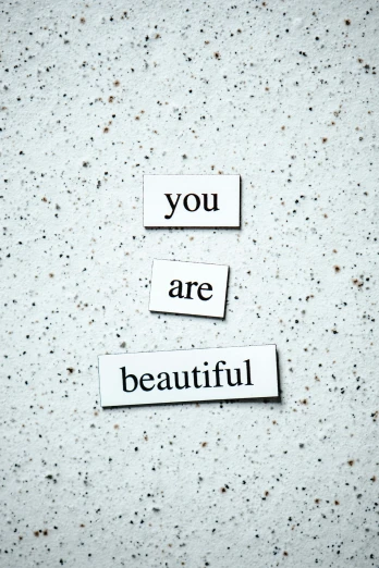 a piece of paper with the words you are beautiful written on it, by Bernie D’Andrea, unsplash, made of all white ceramic tiles, grey, half image, beauty