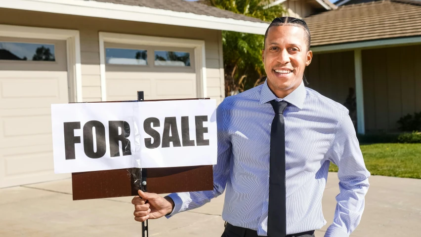 a man holding a for sale sign in front of a house, pexels contest winner, brown skin man with a giant grin, thumbnail, low quality photo, avatar image