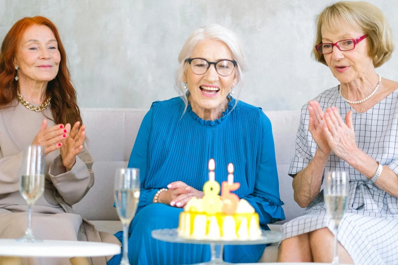 three women sitting on a couch with a cake in front of them, pexels, elderly woman, multiple stories, standing still, pastel'