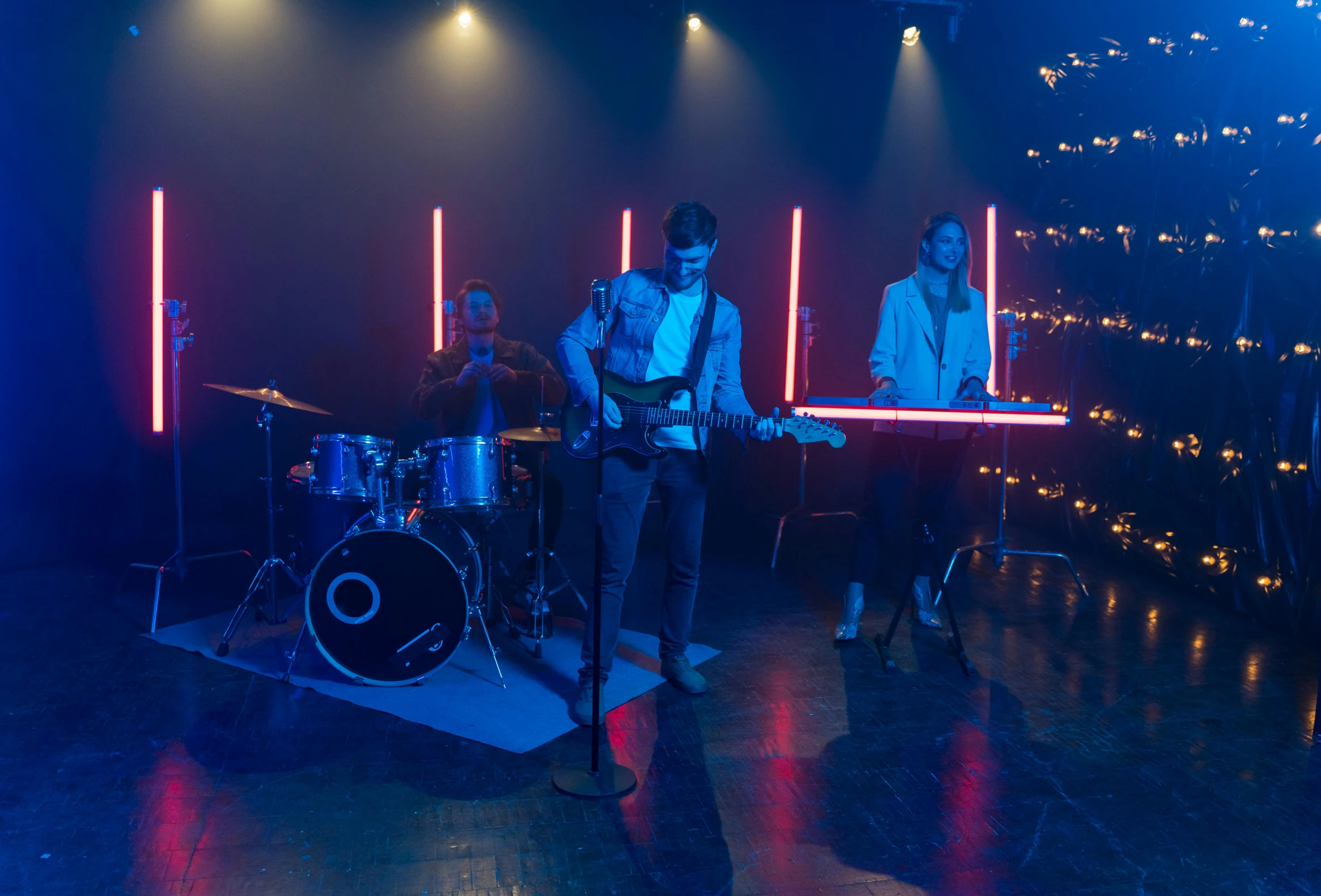 a group of men standing on top of a stage, an album cover, pexels, blue and red lights, tv still frame, band playing instruments, 3 actors on stage