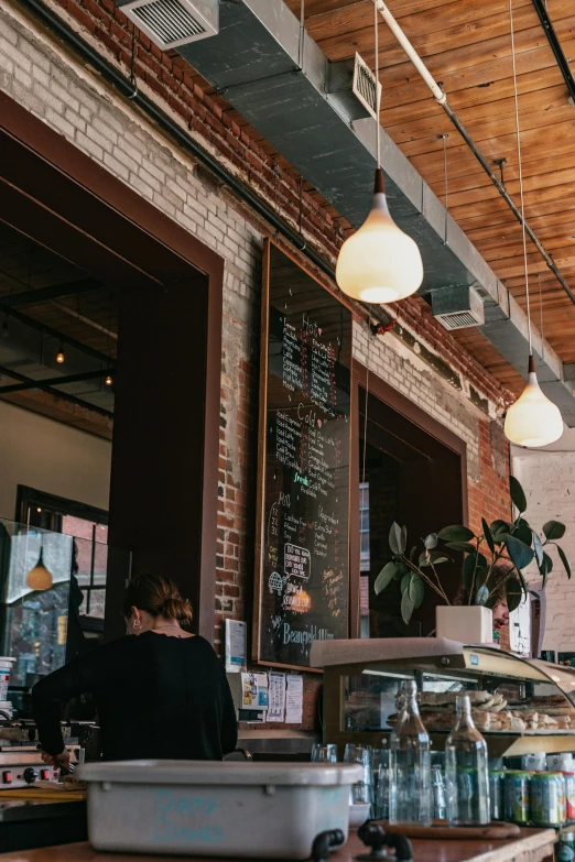 a person sitting at a counter in a restaurant, by Carey Morris, trending on unsplash, things hanging from ceiling, brick building, promo image, cafe