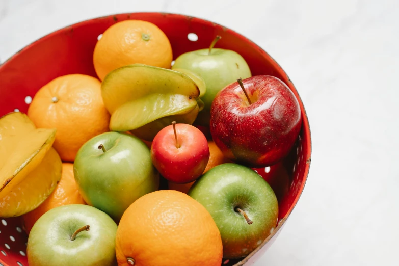 a red bowl filled with lots of different types of fruit, apple orange, zoomed out shot, 🦩🪐🐞👩🏻🦳, medium close shot