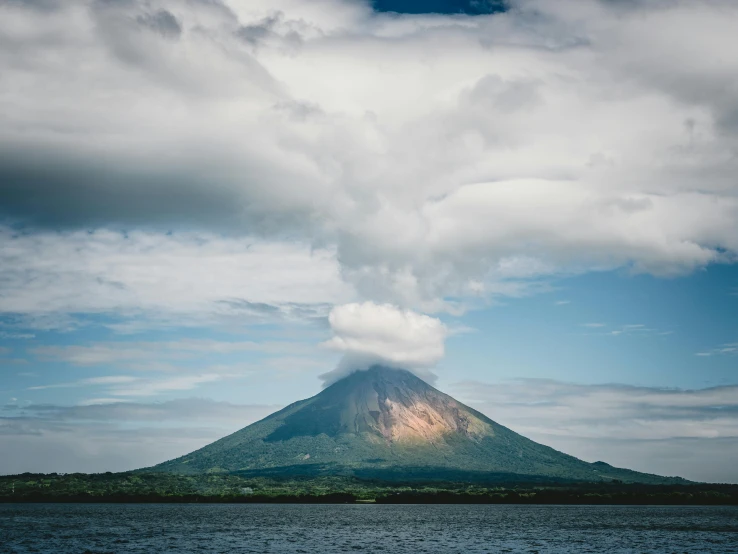 a large mountain towering over a body of water, pexels contest winner, in a volcano, billowing clouds, thumbnail, high resolution photo