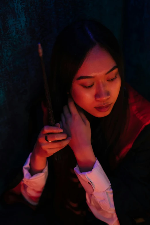 a close up of a person holding a cell phone, an album cover, inspired by Hermione Hammond, pexels contest winner, magical realism, wearing red sorcerers robes, a young asian woman, wands, low-light photograph