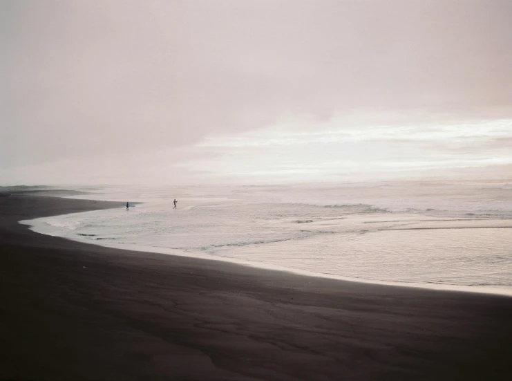 a couple of people standing on top of a beach next to the ocean, by Caro Niederer, minimalism, iceland, dark figures walking, detailed medium format photo, surf photography